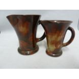 Ewenny Pottery - a milk and cream jug set, the flared cylindrical bodies glazed in a spattered