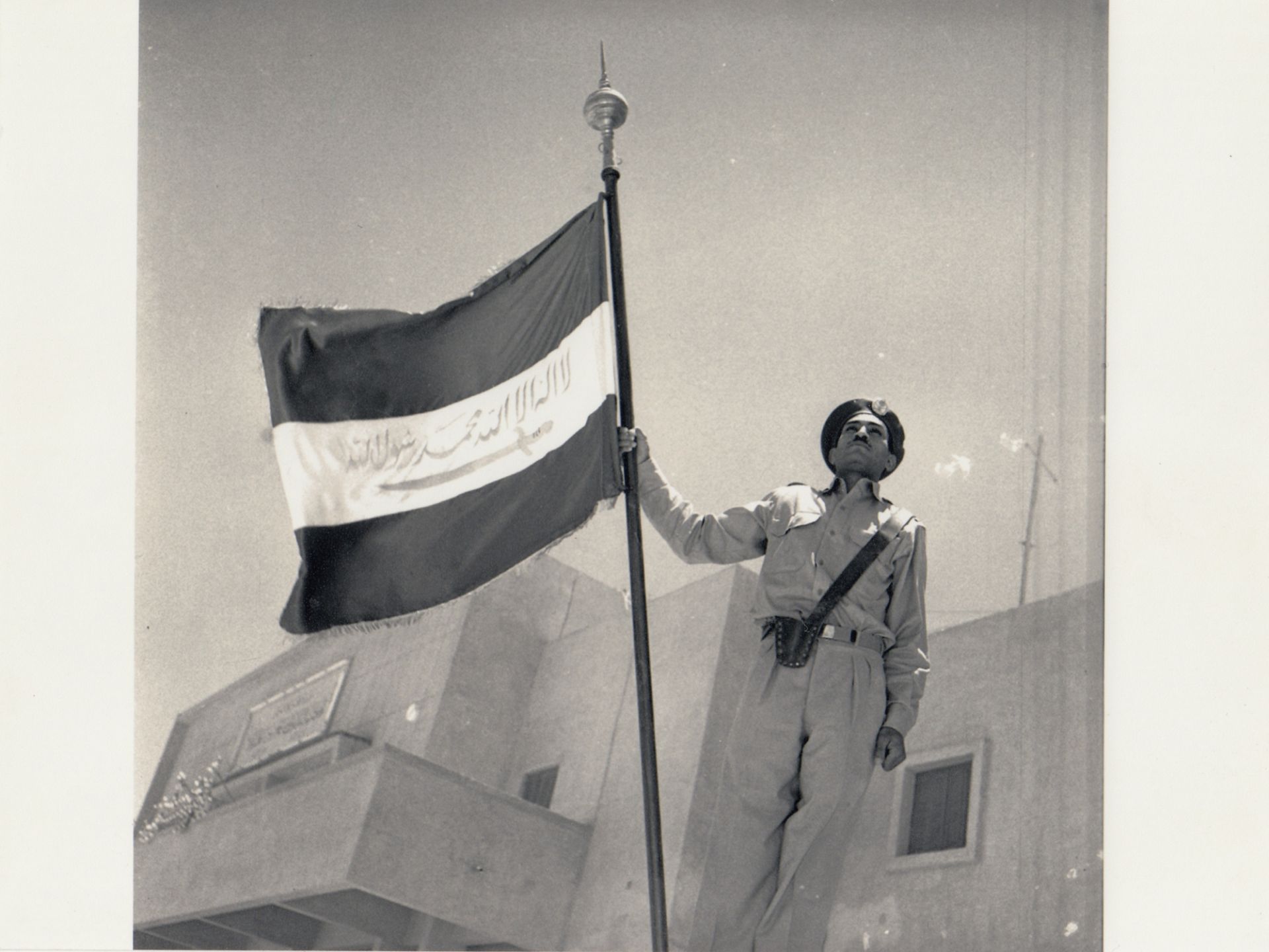 A RARE PHOTOGRAPH OF A PROUD STANDING SAUDI SOLDIER HOLDING AN UNIQUE SAUDI ARABIA FLAG, PROBABLY 19