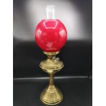 Large vintage brass oil lamp with fitted red globe shade.