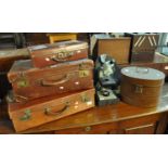 Three vintage leather suitcases, together with an Edwardian tin hat box of oval form and a