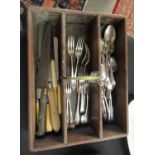 An old wooden cutlery box with a brass handle, containing a selection of cutlery, an old bread knife