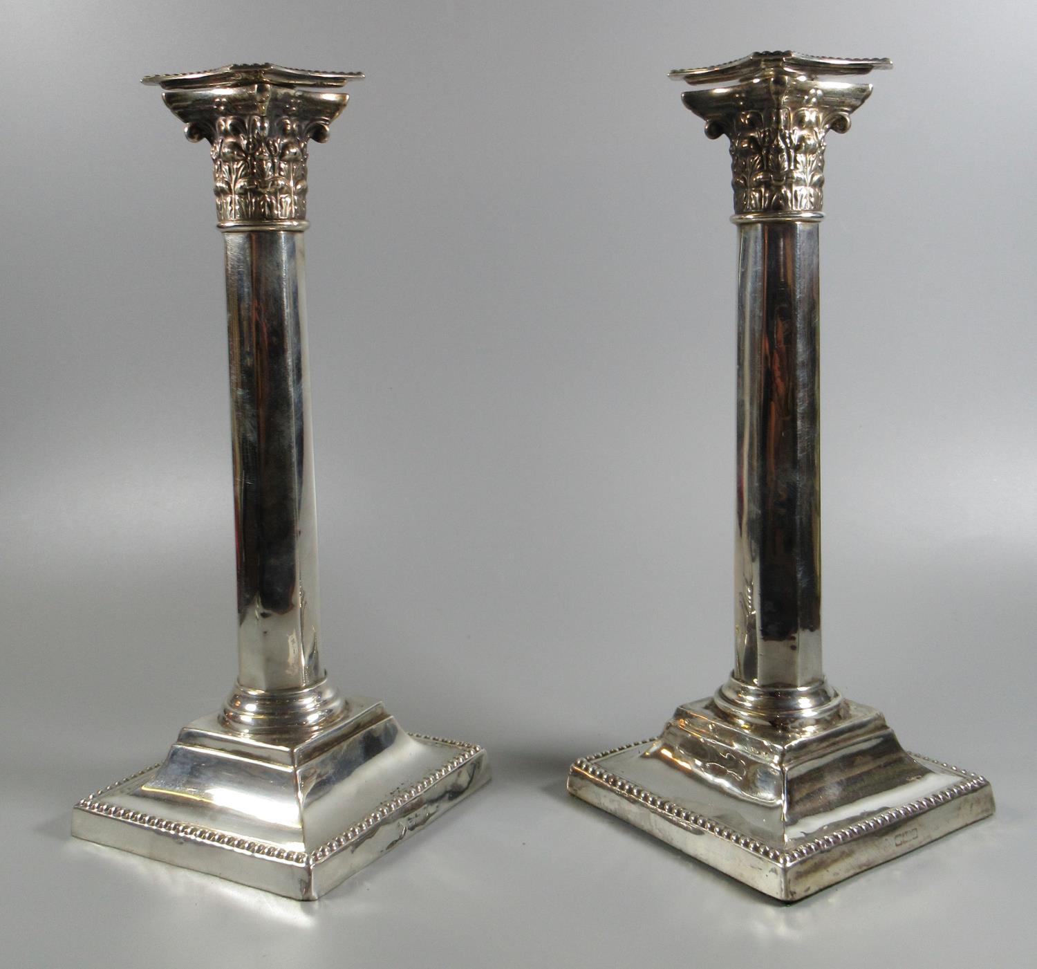 Pair of silver Corinthian column candlesticks on square stepped bases, rubbed hallmarks for