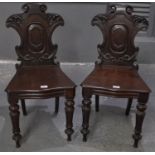 A pair of Victorian mahogany hall chairs with carved foliate and moulded backs, above a serpentine