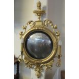 Regency period gilt gesso convex wall mirror with two sconces and flaming urn pediment, scrolled
