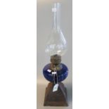 Brass single burner oil lamp with coloured glass reservoir on cast metal base with clear chimney,