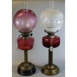 Two similar early 20th Century double oil burners, one with a cranberry etched glass shade and
