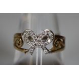 Yellow metal bow ring set with white stones. Ring size O. Approx weight 2.1 grams. (B.P. 21% + VAT)