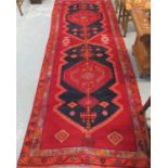 Red ground Persian village runner the borders with stylised flower heads and snakes. 330 x 120cm