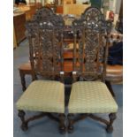 A pair of 20th Century heavily carved high back hall chairs with stuff over seats, standing on