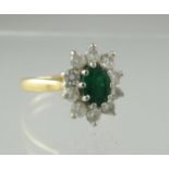 An emerald and diamond ring. The oval emerald approx 6x4.5mm surrounded by ten brilliant cut