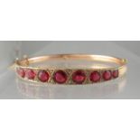 An Edwardian 9ct gold garnet and diamond hinged bangle. The graduated garnets having diamond