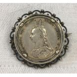 A VICTORIA 1887 SHILLING FASHIONED AS A BROOCH IN WHITE METAL SURROUND