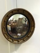 An early 20thc convex wall mirror in reeded ebonised slip and gilded frame with applied sphere