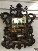 An ornate carved wood Baroque style wall mirror, the rectangular bevelled plate enclosed within a