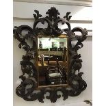 An ornate carved wood Baroque style wall mirror, the rectangular bevelled plate enclosed within a