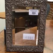 A silver framed mirror, the ornate embossed border enclosing a bevelled plate, with velvet back,