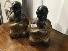 A pair of ebonised and gold painted resin figures of Buddhist monks