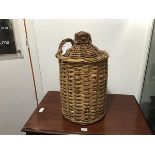 A large glazed stoneware flagon, within a wicker basket, with handle and woven cap (lacking stopper)