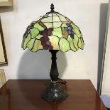 A Tiffany style bronzed metal base table lamp with leaded glass scalloped bordered vine leaf and