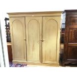 A Victorian stripped pine three door wardrobe, the projecting cornice above an open hanging space