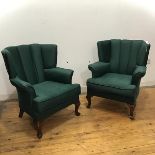 A pair of low armchairs, c.1940, each with wing back and detachable cushion, upholstered in a