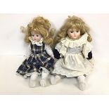 A pair of bisque dolls, both with blonde hair and blue eyes, one dressed in lace and velvet, the