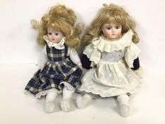 A pair of bisque dolls, both with blonde hair and blue eyes, one dressed in lace and velvet, the