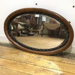 An early 20thc walnut framed wall mirror, the oval bevelled plate within an ebonised border and
