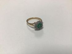 A 9ct gold emerald and diamond cluster ring with seven emeralds enclosed within a surround of nine