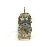 A modern reproduction brass lantern style clock with silvered dial and roman numerals, raised on bun