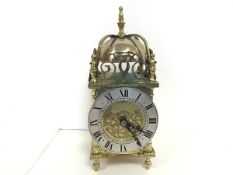 A modern reproduction brass lantern style clock with silvered dial and roman numerals, raised on bun