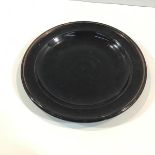 A studio porcelain plate, probably Japanese, in a black/brown glaze, the well spirally moulded, with