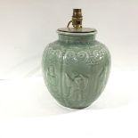 A Chinese celadon glazed jar, possibly a wine jar, moulded with panels enclosing figures beneath a