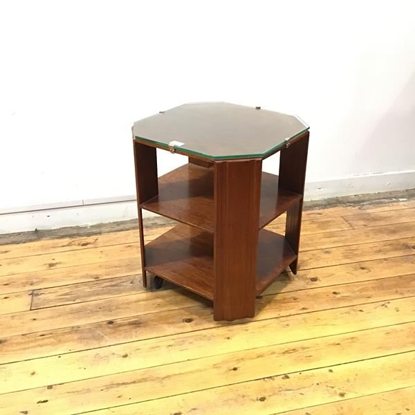 A 1930s mahogany bookstand, the octagonal top with glass cover above two open shelves, within canted