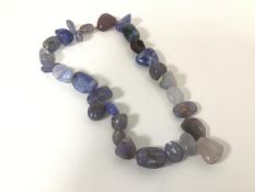 A polished stone necklace comprising primarily blue toned stones of oval shape, with a screw