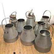 A collection of eight milk churns, seven of identical conical form, one with a mechanical lid and