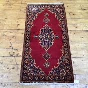 A small woven wool rug of Persian design, the tomato red field decorated with indigo medallion and