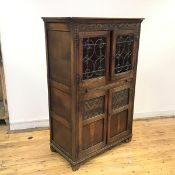 An Ercol style oak cabinet of 17thc inspiration, the carved frieze above a pair of leaded glazed