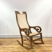 A late 19thc simulated walnut rocking chair, the arched top rail above a woven cane back and seat,