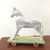 A hand carved and painted model of a horse, with woven wool tail and leather ears, raised on a green