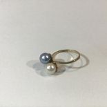 A cultured pearl dress ring, the two pearls, one white, the other grey, in a crossover setting, on a