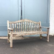 A teak garden bench, with undulating top rail and shaped spar back, on a slatted seat with square