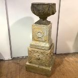A composition garden urn, decorated with ribbon swags, raised on a socle and mounted on two