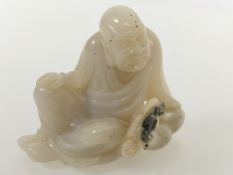 A Chinese celadon jade carving of a seated man, one hand resting on his knee. 4.75cm by 5.5cm