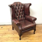 A George III style wing back armchair, upholstered in deep plum hide, the arched back with butttoned