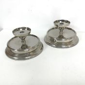 A pair of metal circular candleholders, the central drip tray above a lower tier with plain frieze