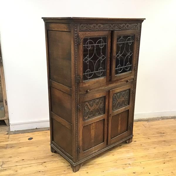 An Ercol style oak cabinet, in 17thc style, with a carved frieze above a pair of leaded glazed