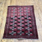 A hand knotted wool rug of Turkoman design, the madder field with a grid design enclosing ivory