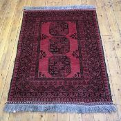 A hand woven wool Afghan rug, the madder field with three elephant's foot gulls, enclosed by