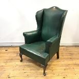An Edwardian leather upholstered wing armchair, the shaped back and outswept arms above a padded